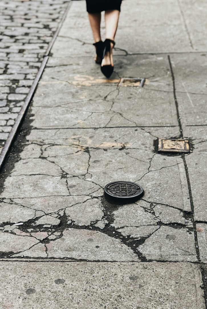 A woman in high heels walking down a cracked sidewalk in Tulsa Oklahoma that's in desperate need of concrete repair.